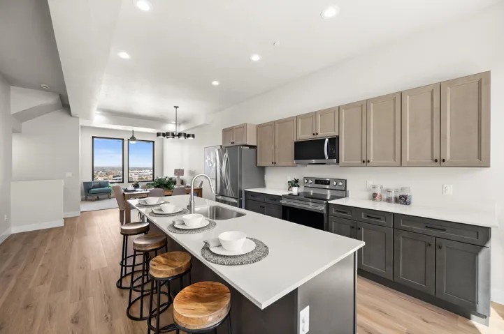 Open-concept kitchen featuring an oversized island with an undermount sink, light wood-finish flooring, recessed lighting, and two-tone cabinetry with black hardware