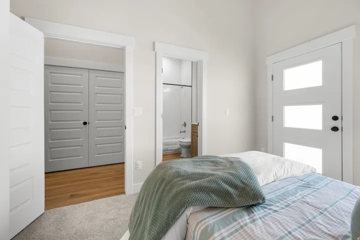 Light-filled room featuring a modern door with three frosted glass panels, an open doorway revealing a bathroom with a shower-tub combination, and a separate doorway leading to a room with wood-finish flooring and grey bifold doors
