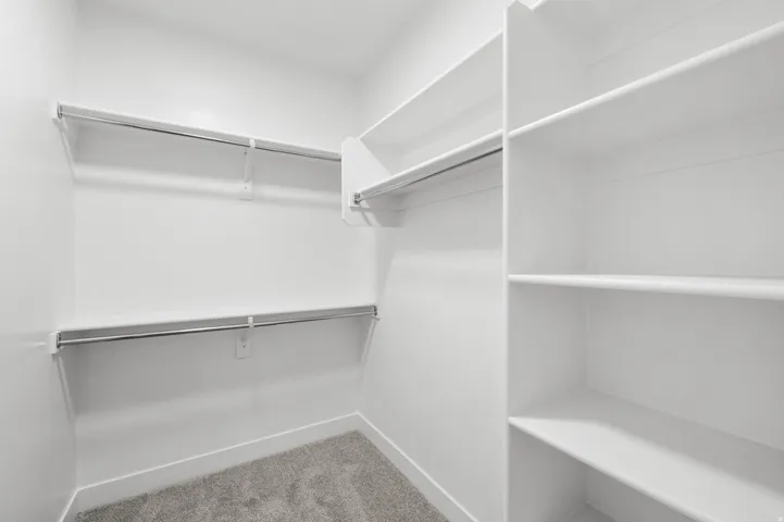 Walk-in closet featuring built-in shelving, dual hanging rods, and grey carpeting