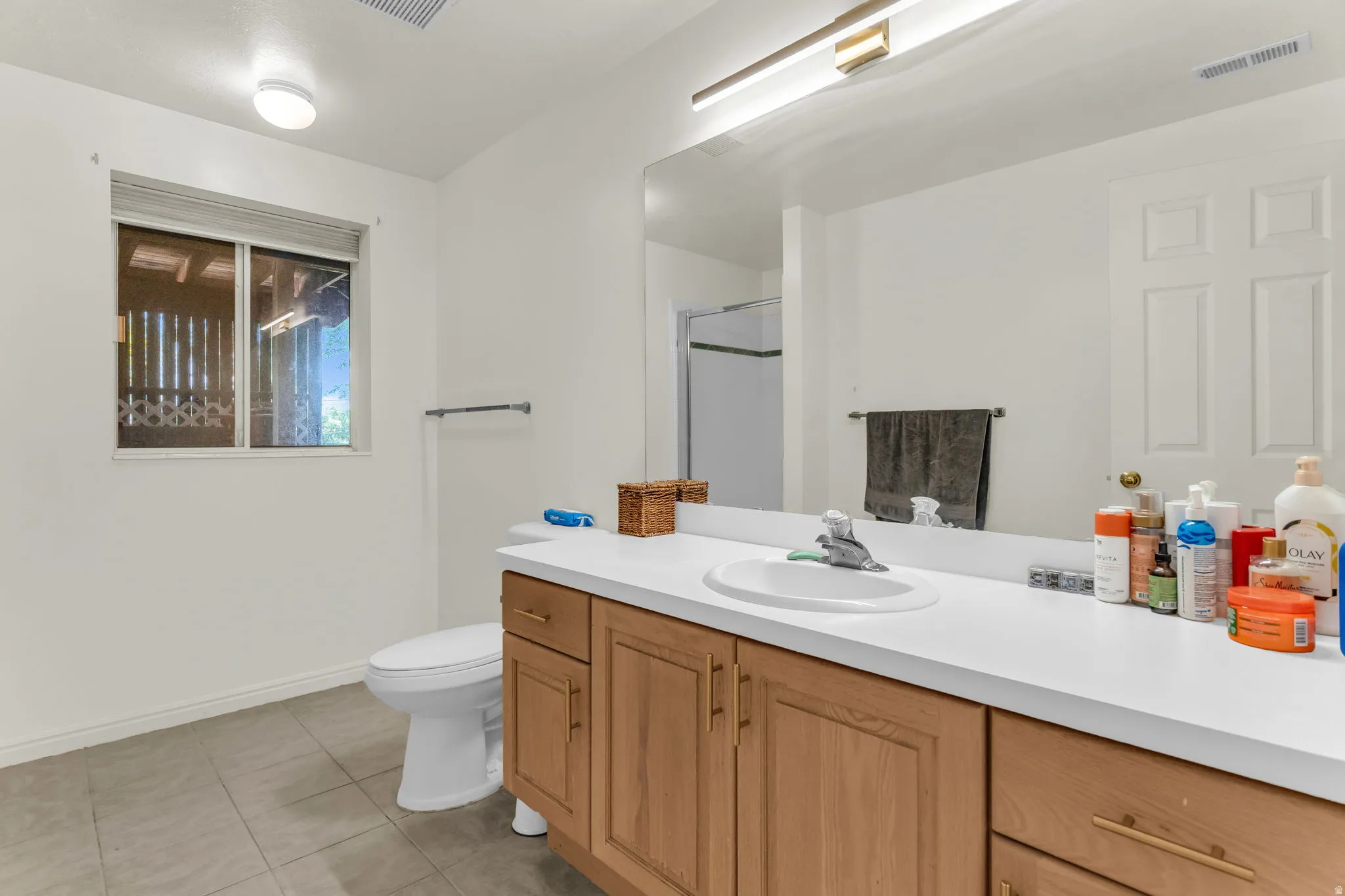 Bathroom featuring a light wood-finish vanity with a white countertop and integrated sink, a large wall-mounted mirror, and tile flooring