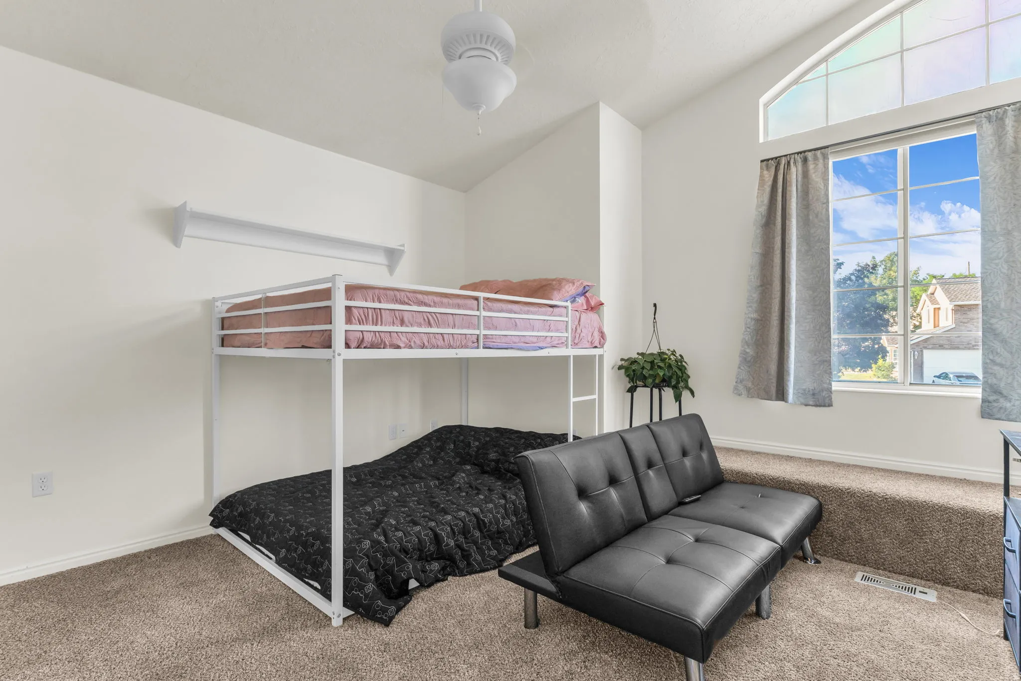 Vaulted ceiling room featuring a large arched window with clear glass panes, light-colored carpeting, and a built-in wall shelf
