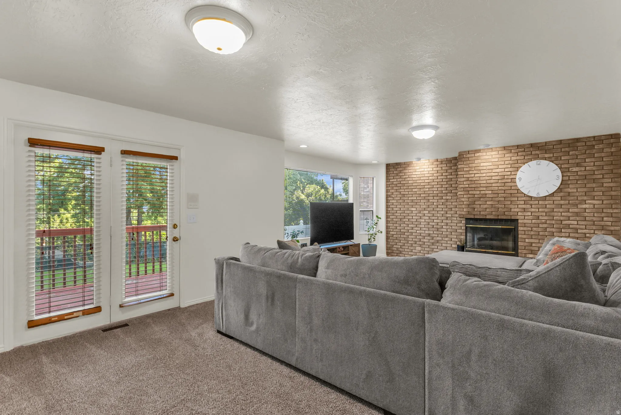 Living area featuring a brick accent wall with an integrated fireplace, plush carpet flooring, and recessed lighting