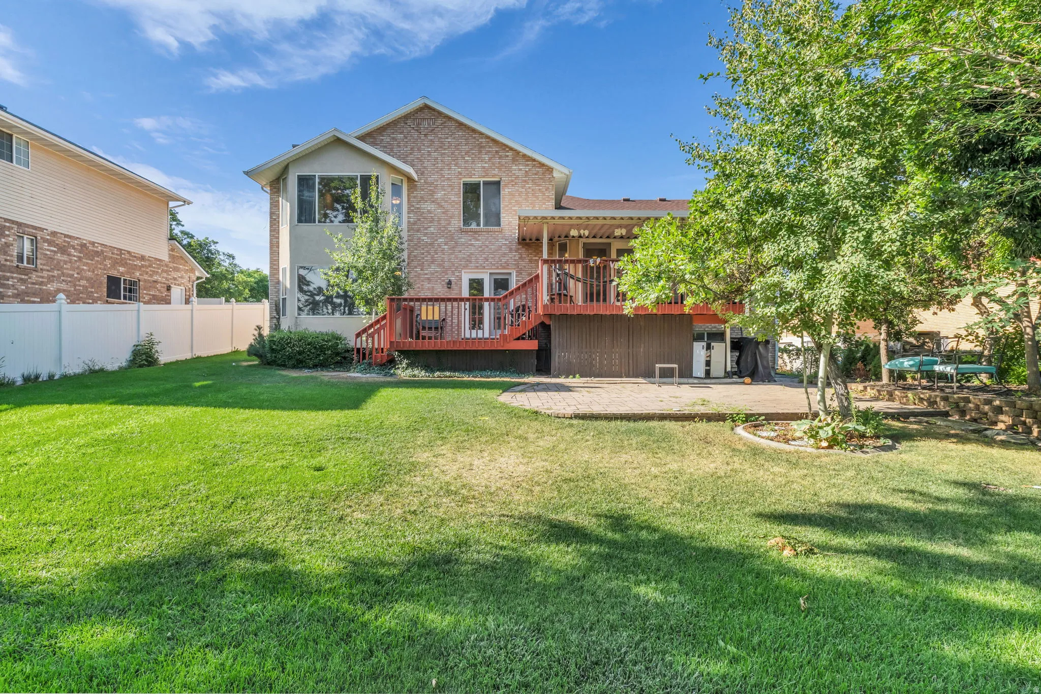 Spacious backyard featuring a large green lawn, a multi-level deck with red wood-finish railings, and a lower-level paver patio