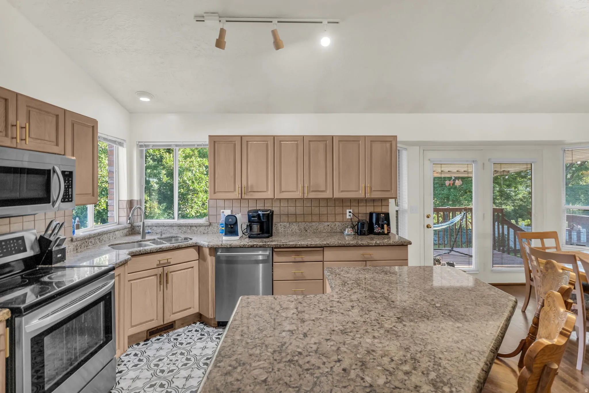 Kitchen featuring granite countertops, stainless steel appliances, wood cabinetry, patterned tile flooring, and a glass-paneled door leading to an outdoor deck