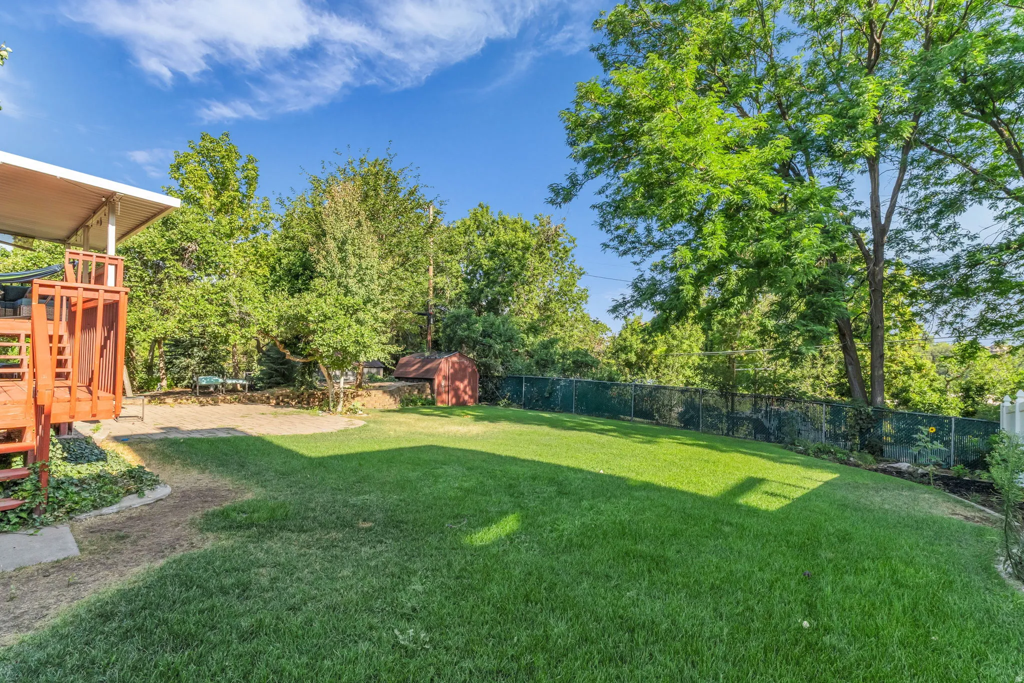 Expansive backyard featuring a large green lawn, mature trees, a red wooden storage shed, and a privacy fence