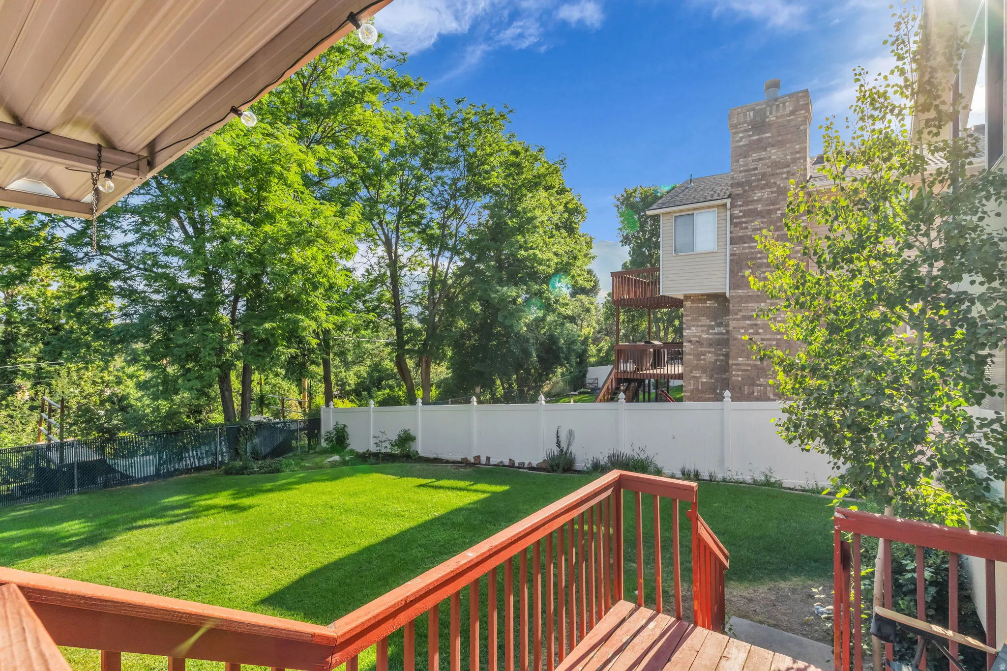 Spacious grassy yard with a white privacy fence and mature perimeter trees
