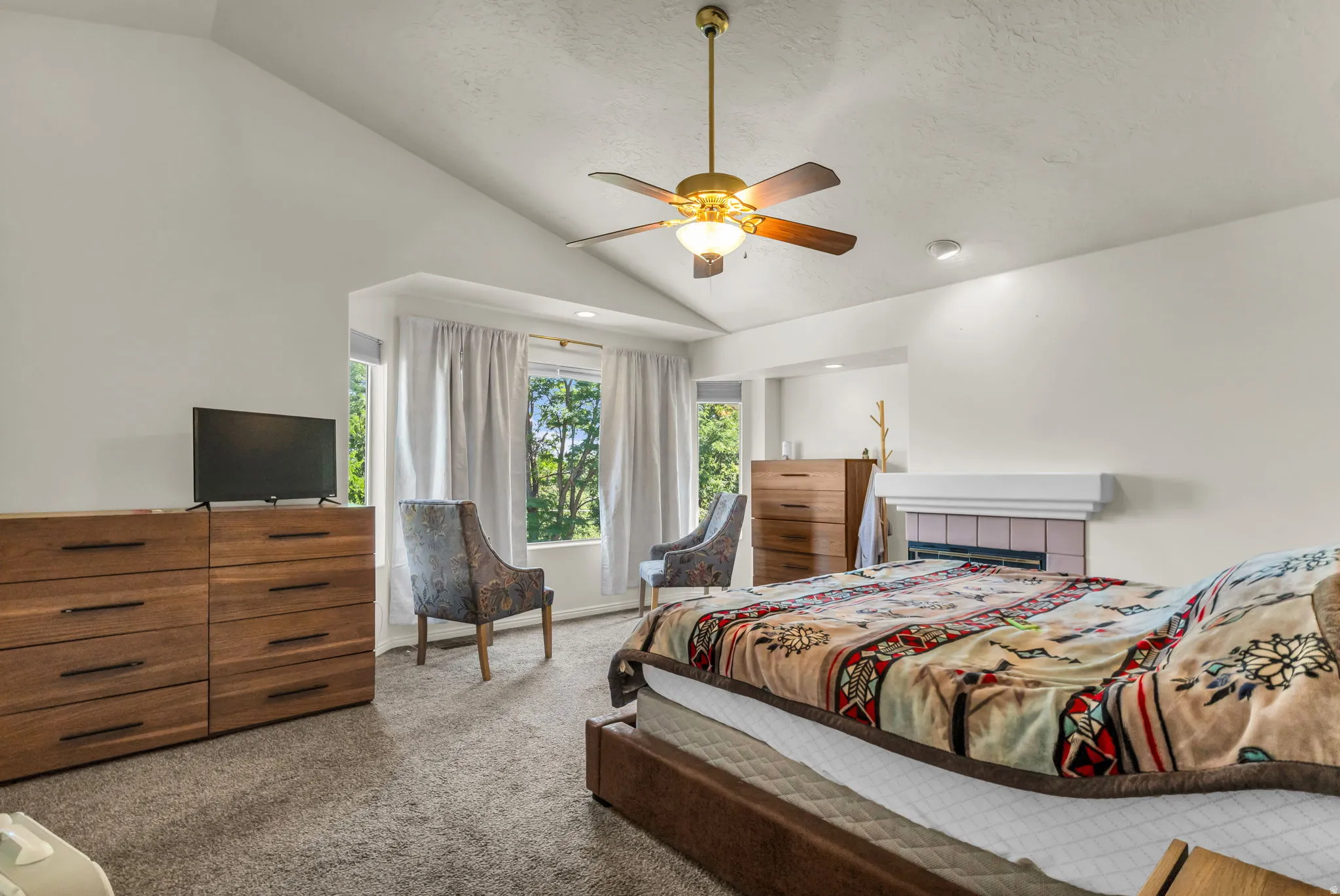 Vaulted ceilings with a ceiling fan, bay windows, built-in fireplace with tile surround, and neutral carpeting
