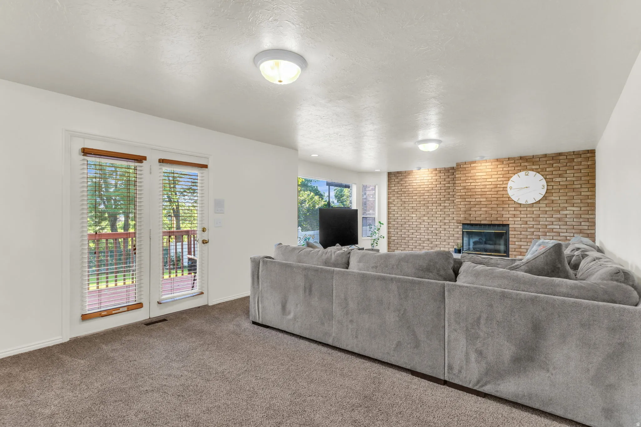 Living area featuring neutral carpeting, a brick accent wall with a fireplace, and a glass-paneled door opening to an exterior deck