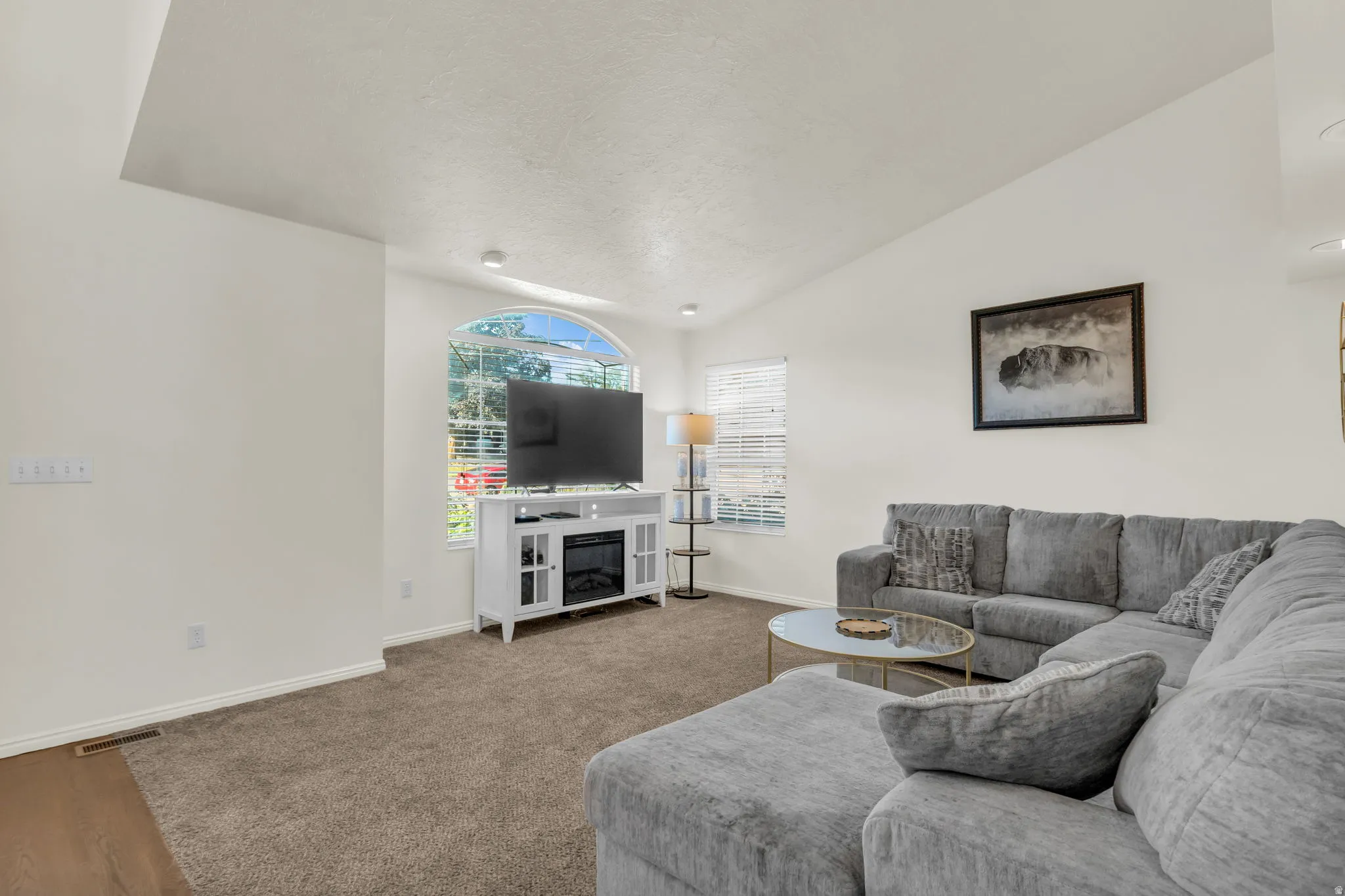 Spacious living area featuring vaulted ceilings, a large arched window with blinds, recessed lighting, and a built-in media console with an electric fireplace