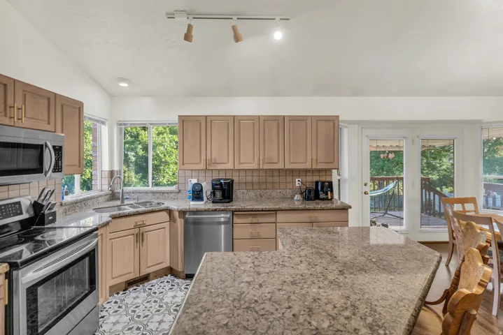 Kitchen featuring granite countertops, stainless steel appliances, wood cabinetry, patterned tile flooring, and a glass-paneled door leading to an outdoor deck