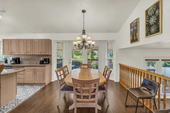 Open-concept living space featuring a dining area with a multi-light chandelier, double doors to an exterior deck, wood-finish flooring, and a railing overlooking a lower level