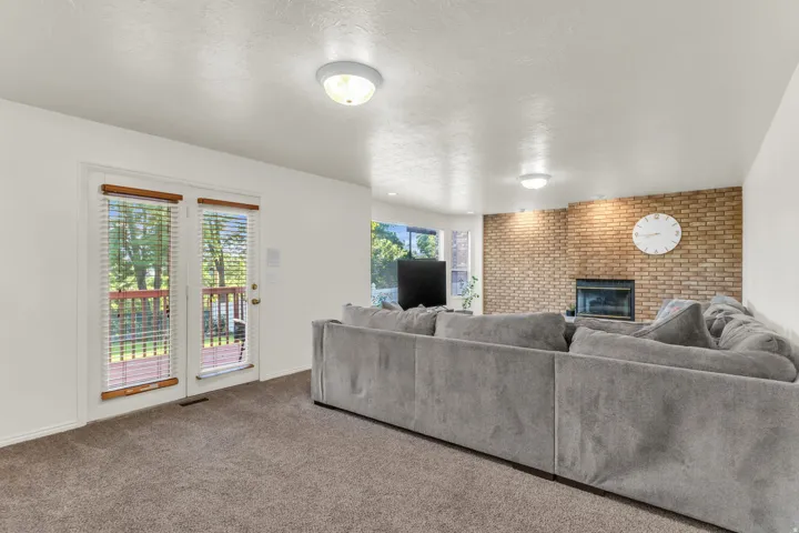Living area featuring neutral carpeting, a brick accent wall with a fireplace, and a glass-paneled door opening to an exterior deck