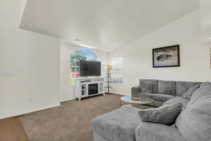 Spacious living area featuring vaulted ceilings, a large arched window with blinds, recessed lighting, and a built-in media console with an electric fireplace
