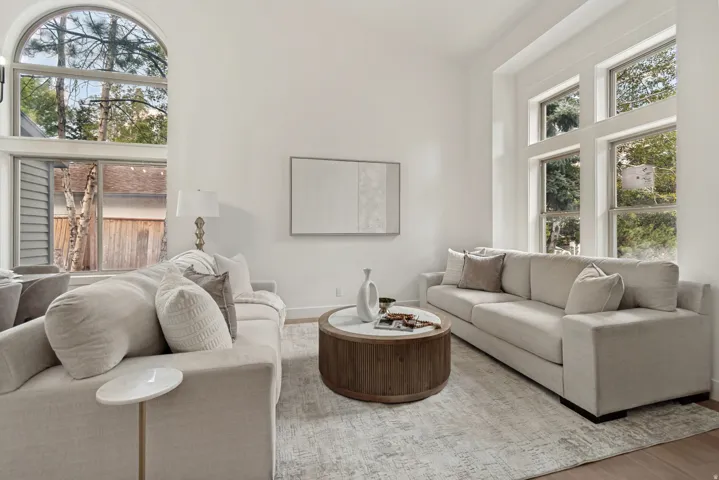 Living area featuring high ceilings, a prominent arched window, additional large windows, wood-finish flooring, and light-toned walls