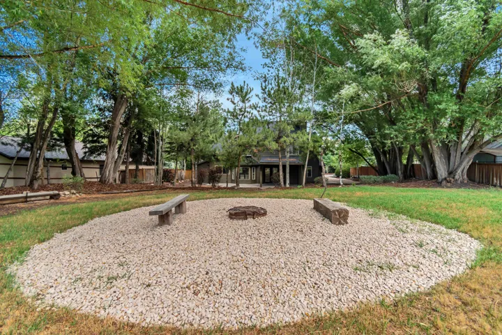 Expansive backyard featuring a central gravel fire pit area with two wooden benches, surrounded by a manicured lawn