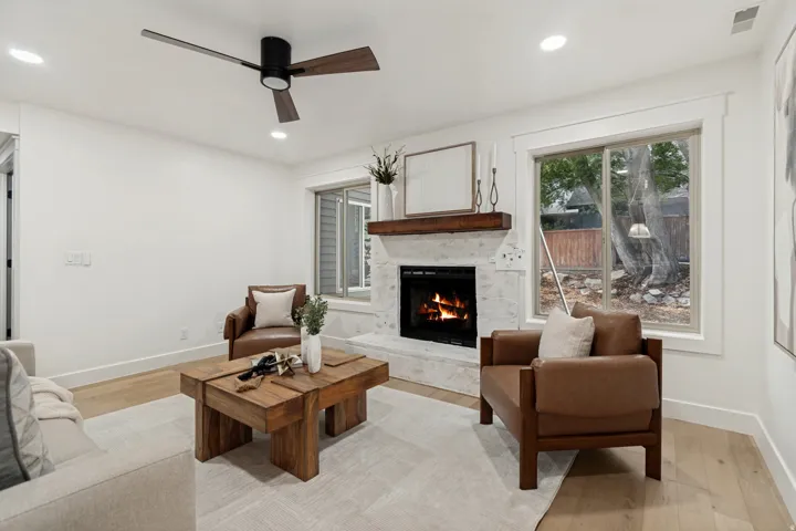 Living area featuring a white brick fireplace with a wood mantle, wood-finish flooring, recessed lighting, a ceiling fan, and large windows