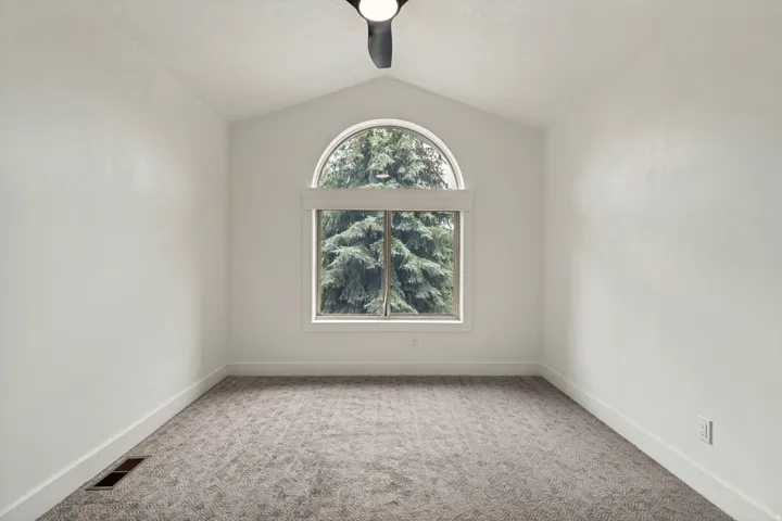 Vaulted ceiling room featuring a large arched window, neutral-toned carpet, white trim, and a ceiling fan