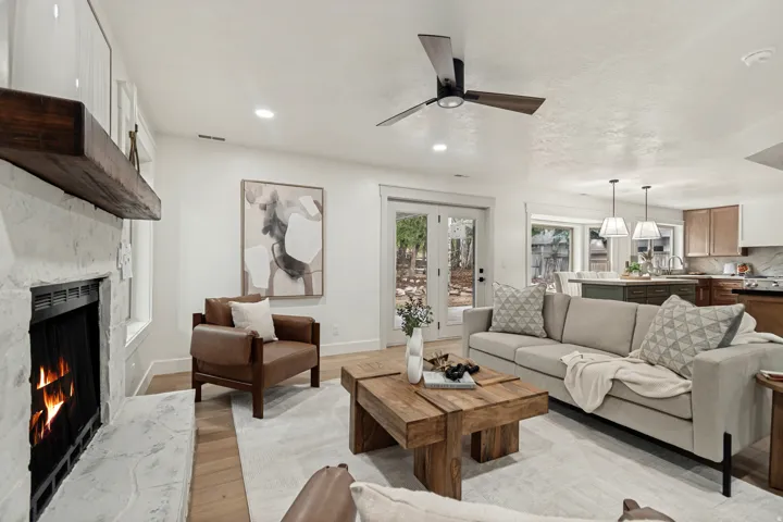 Open concept living area featuring a whitewashed stone fireplace with a substantial wood mantle, wood-finish flooring, a contemporary ceiling fan, recessed lighting, and French doors leading to exterior space