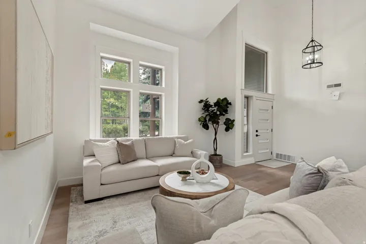 Spacious living area featuring high ceilings, tall windows with white trim, wood-finish flooring, and a modern entry door with frosted glass panels