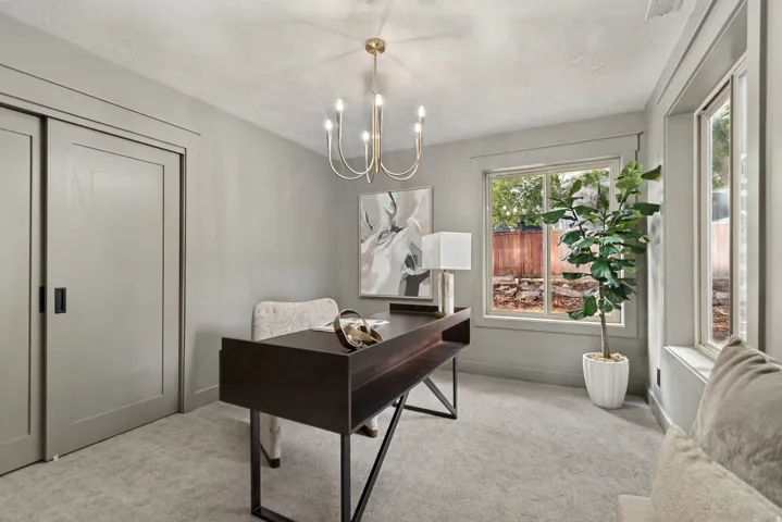 Neutral-toned room featuring a gold-finish chandelier, light gray carpeting, and two large windows providing natural light