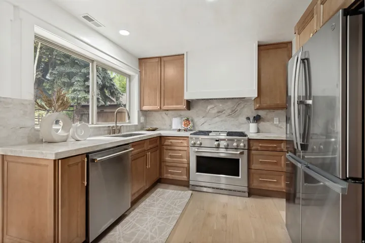 Kitchen featuring light wood cabinetry, stainless steel appliances, light-toned countertops, a light-toned backsplash, and wood-finish flooring