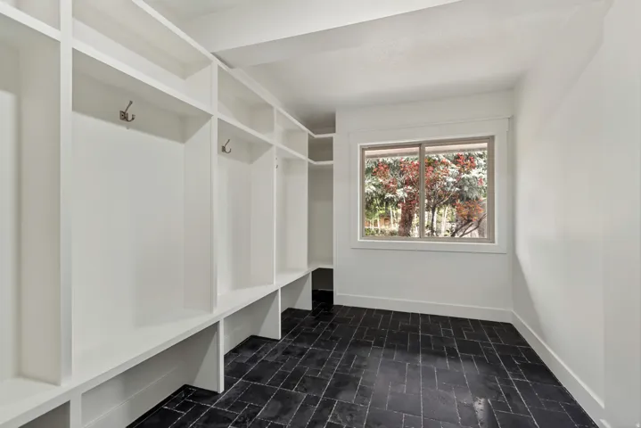 Dedicated mudroom featuring extensive built-in storage cubbies with integrated hooks and bench seating, complete with a large window and dark herringbone tile flooring