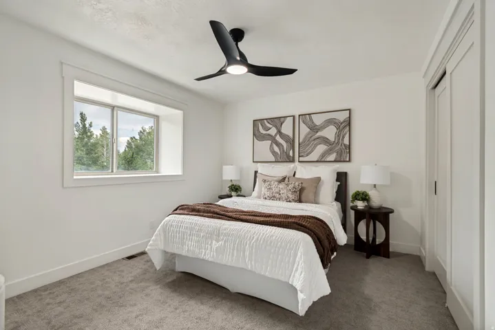 Bedroom featuring a large recessed window with exterior tree views, a ceiling fan with integrated lighting, white walls, and gray carpet flooring