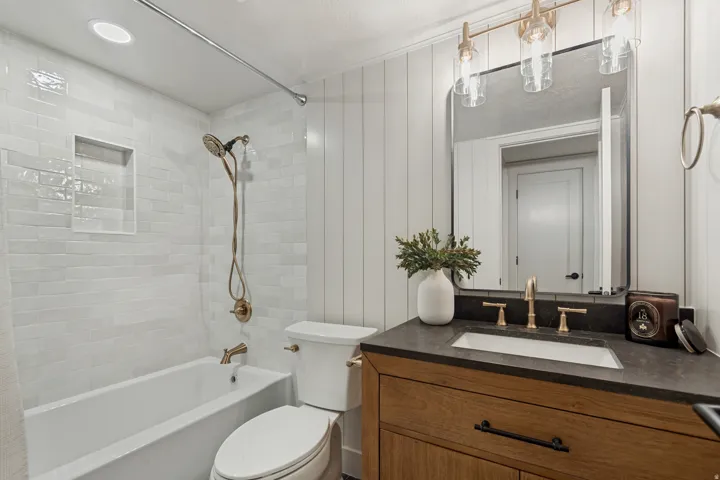 Bathroom featuring a wood-finish vanity with an integrated sink, dark countertop, and brass-finish fixtures