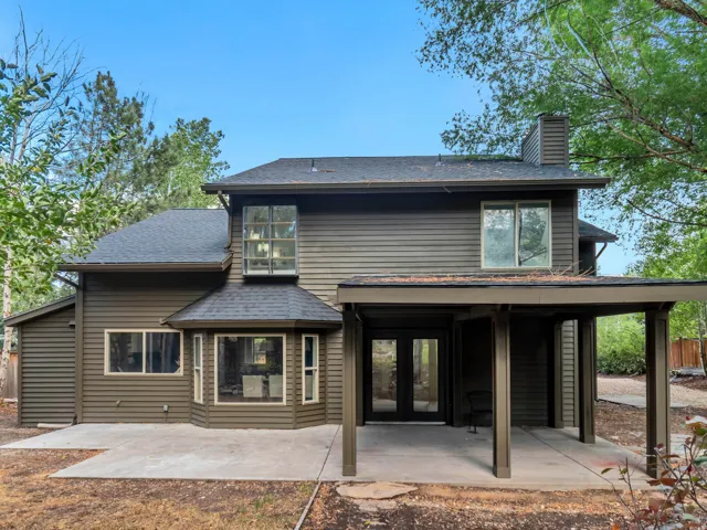 Rear exterior of a two-story residence with dark siding, featuring multiple windows, a covered patio area, and an additional concrete patio space