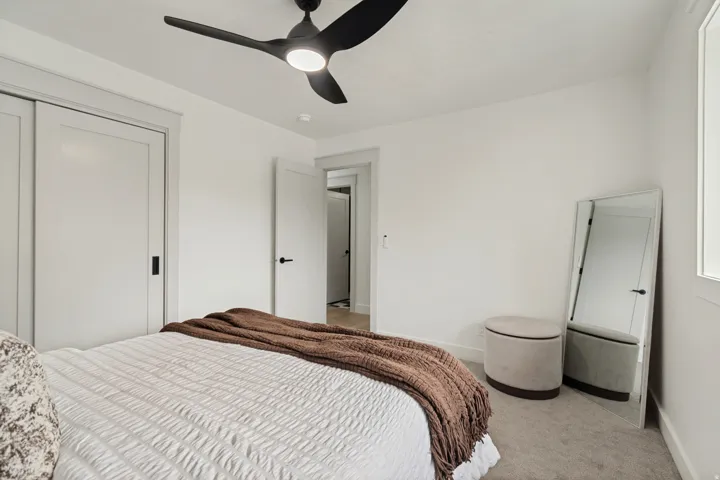 Bedroom with modern ceiling fan, gray carpeting, white walls, and a white interior door with black hardware