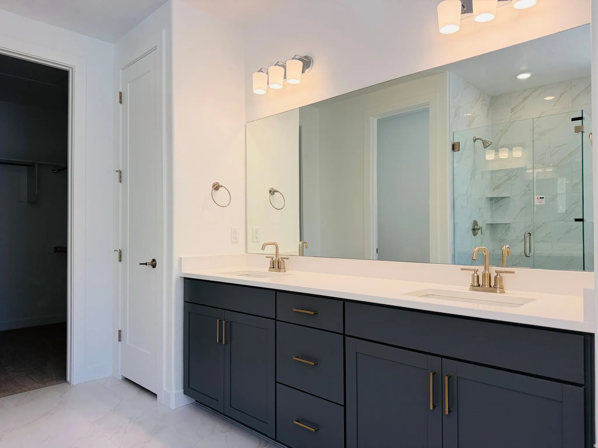 Bathroom featuring a dual-sink vanity with dark cabinetry, white countertops, and gold-toned fixtures