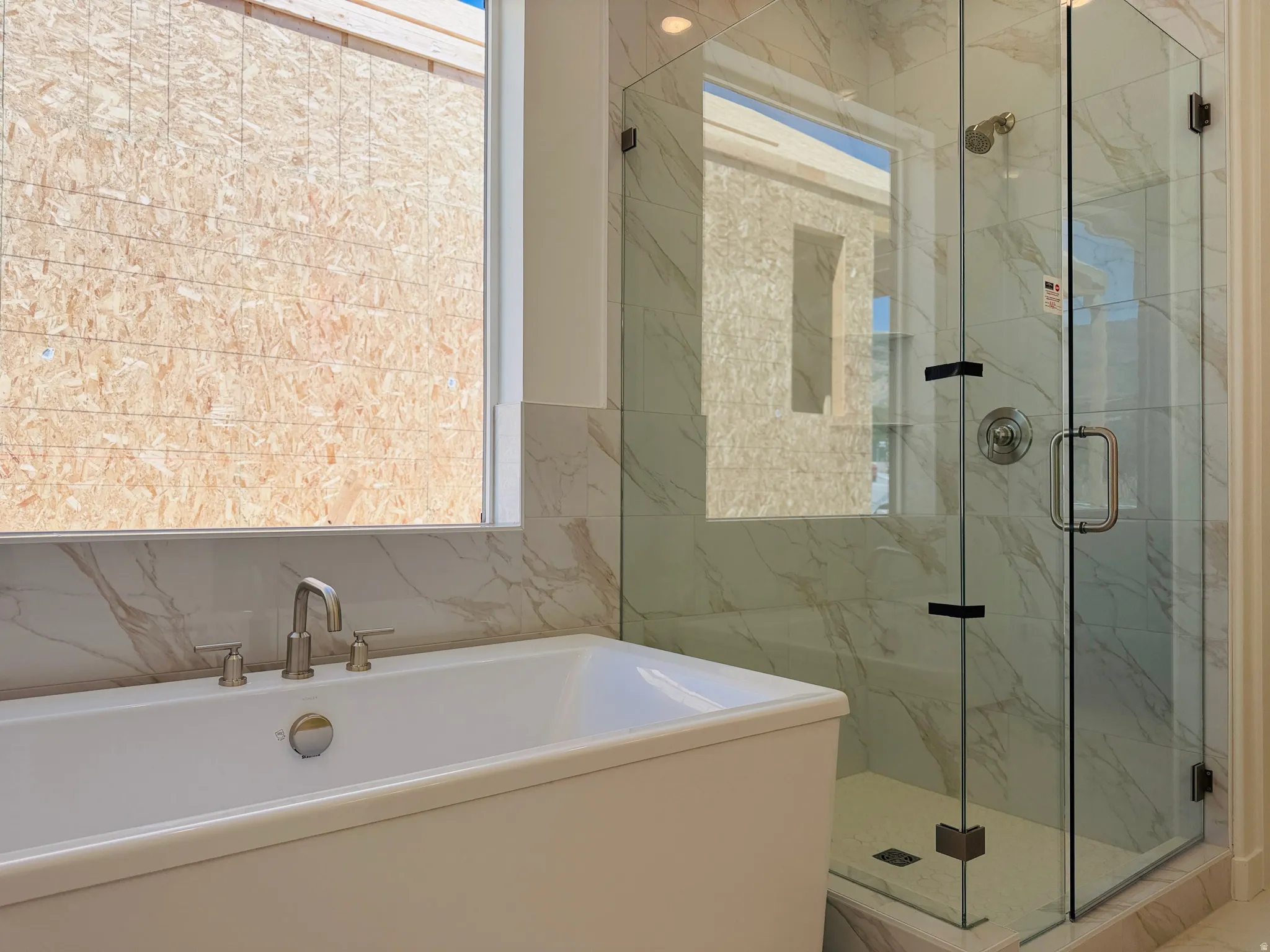 Freestanding soaking tub with brushed nickel faucet, large walk-in shower with glass enclosure, and white marble-look wall tiling