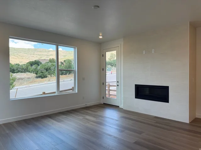 Spacious room featuring wood-finish flooring, a large multi-pane window, and a contemporary linear fireplace with a textured surround