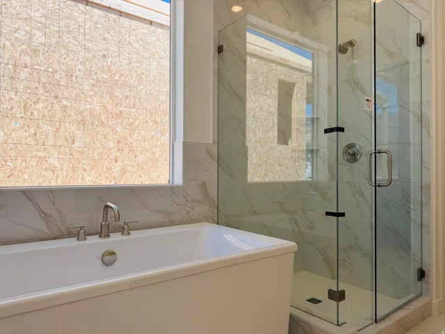 Freestanding soaking tub with brushed nickel faucet, large walk-in shower with glass enclosure, and white marble-look wall tiling