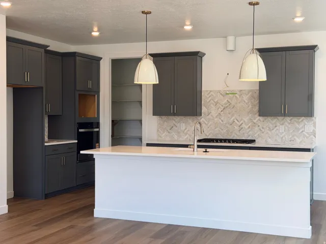 Modern kitchen featuring dark grey cabinetry, white countertops, and a herringbone pattern tile backsplash