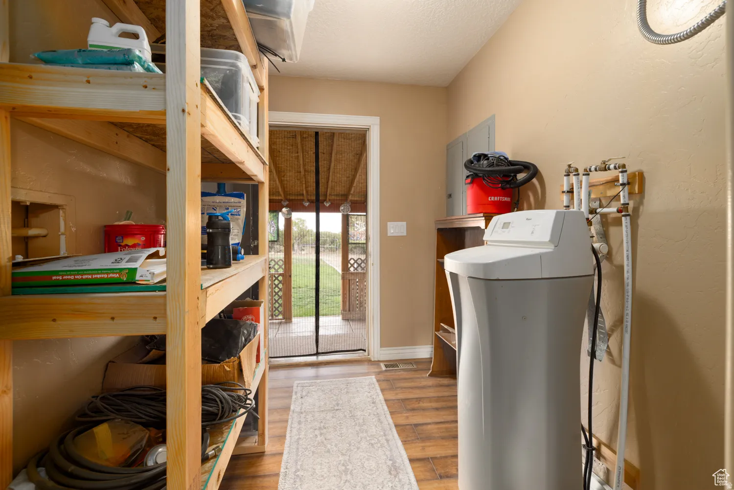 Utility area featuring wood-finish flooring, built-in wooden shelving, and a water treatment system