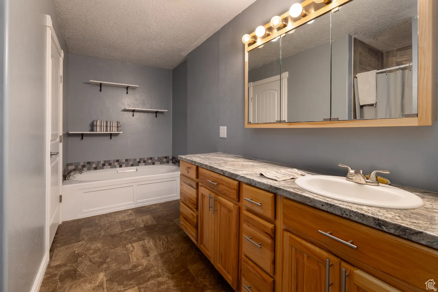 Spacious bathroom featuring a long wood vanity with an integrated sink and chrome faucet, flanked by a built-in soaking tub with a tiled surround