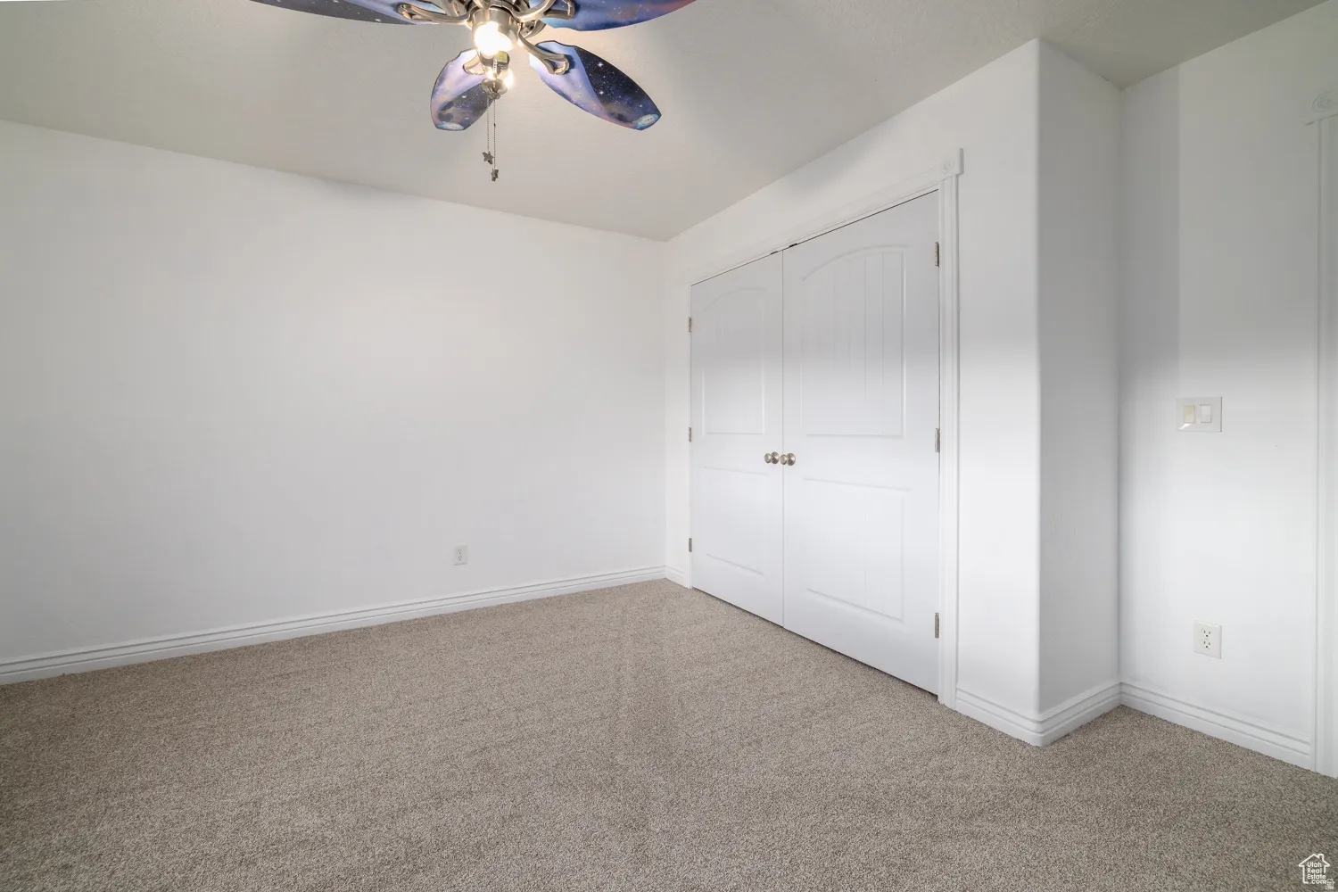 Carpeted room featuring a ceiling fan, white baseboards, and dual paneled doors
