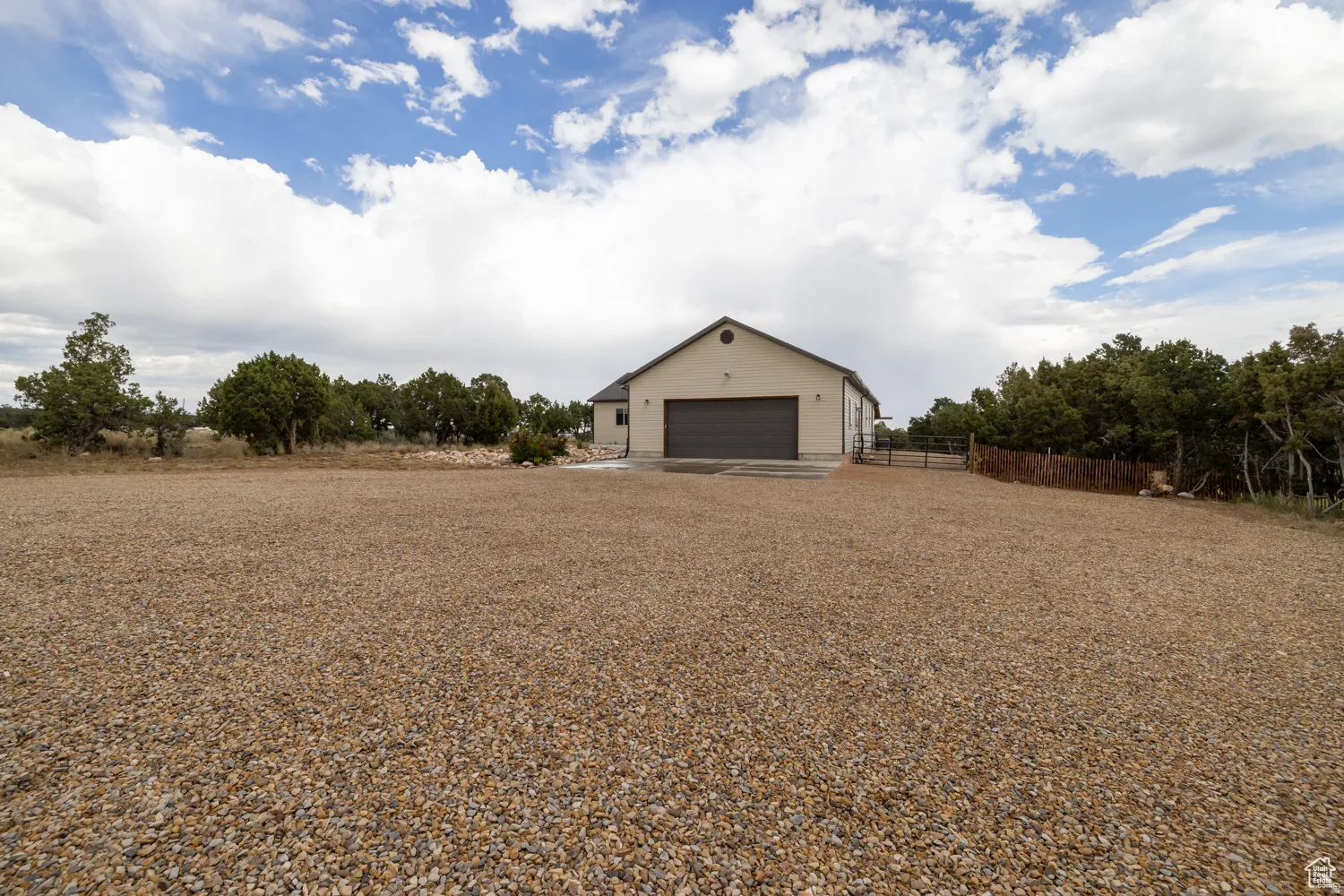 Gravel driveway leading to a neutral-toned building with a prominent dark-colored garage door and a side entrance