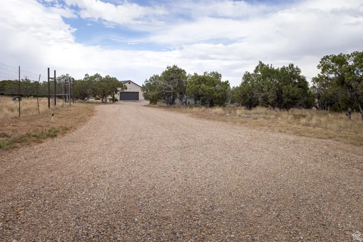 Gravel driveway leading to a residence featuring a tan stucco exterior and an attached garage with a dark-colored door