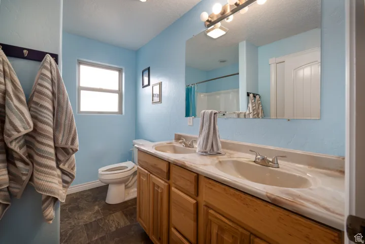 Bathroom featuring a double vanity with wood-finish cabinetry, a large wall-mounted mirror, a built-in toilet, and patterned tile flooring