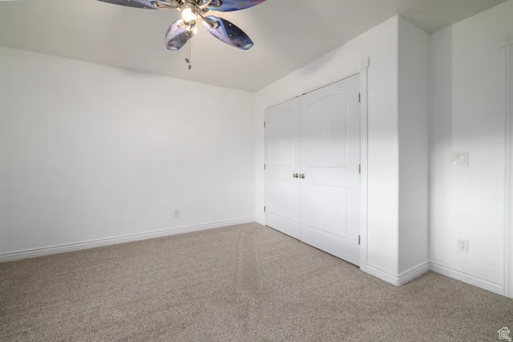Carpeted room featuring a ceiling fan, white baseboards, and dual paneled doors