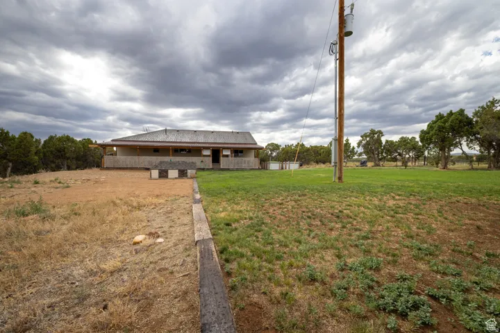 Ranch-style residence featuring a covered porch with wooden support beams, a metal roof, and an expansive lawn