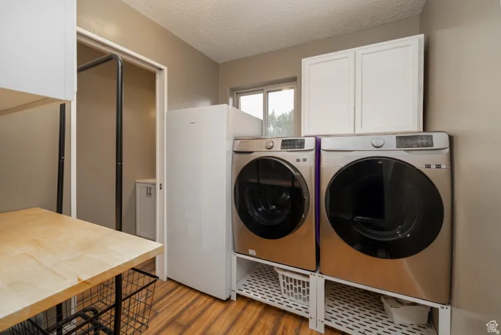 Dedicated laundry area featuring wood-finish flooring, white upper cabinetry, and a light wood-finish countertop