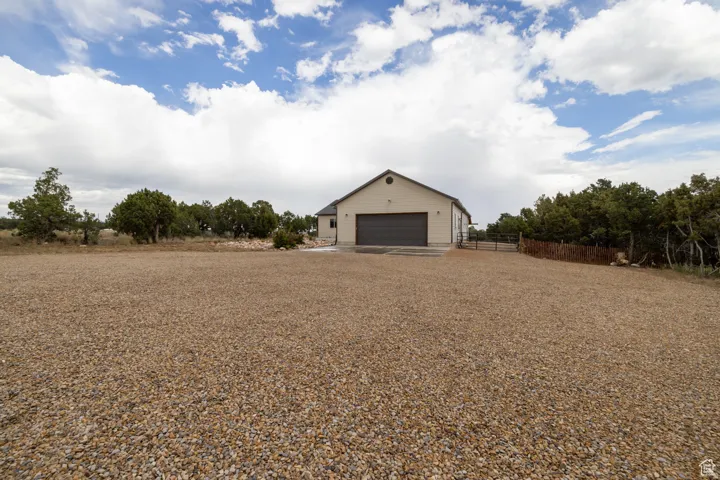 Gravel driveway leading to a neutral-toned building with a prominent dark-colored garage door and a side entrance