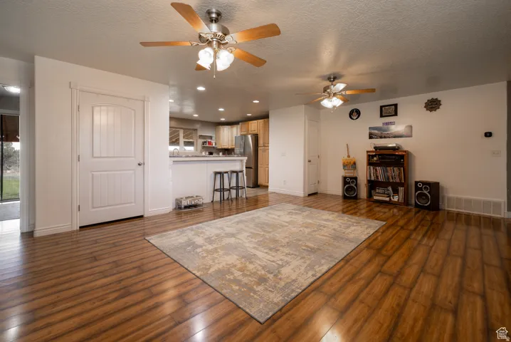 Open-concept interior featuring wood-finish flooring, two ceiling fans with integrated lighting, and a kitchen bar with a light-toned countertop