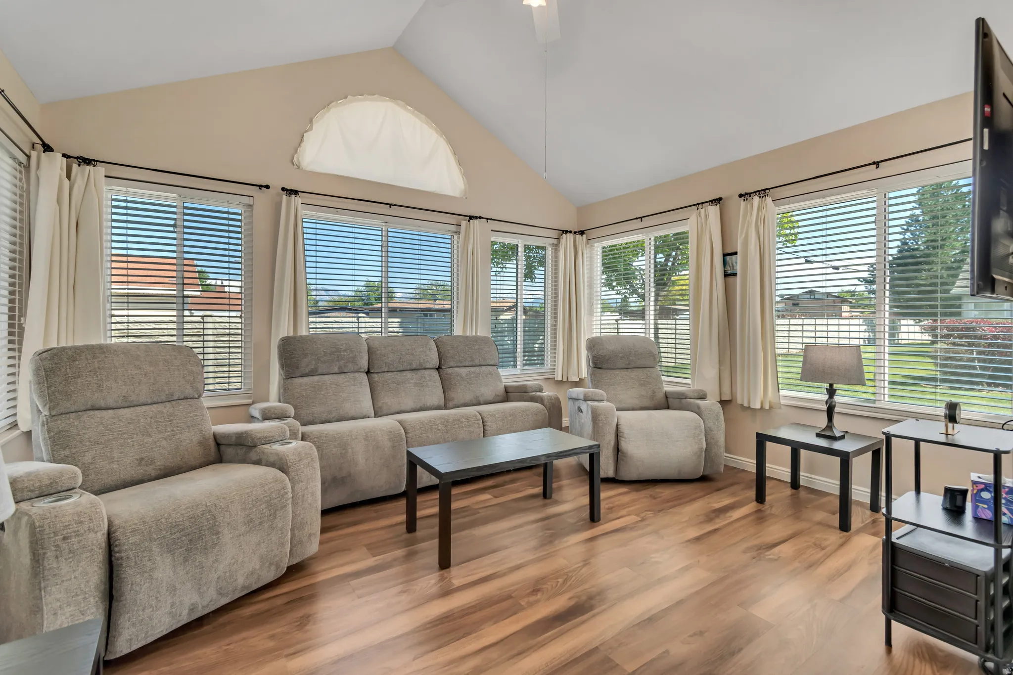 Spacious living area featuring vaulted ceilings, wood-finish flooring, and multiple large windows with blinds
