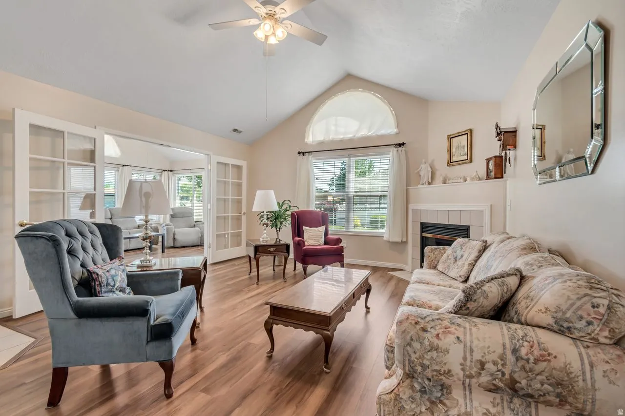 Living area featuring vaulted ceilings, wood-finish flooring, and a fireplace with a white mantel and tiled surround