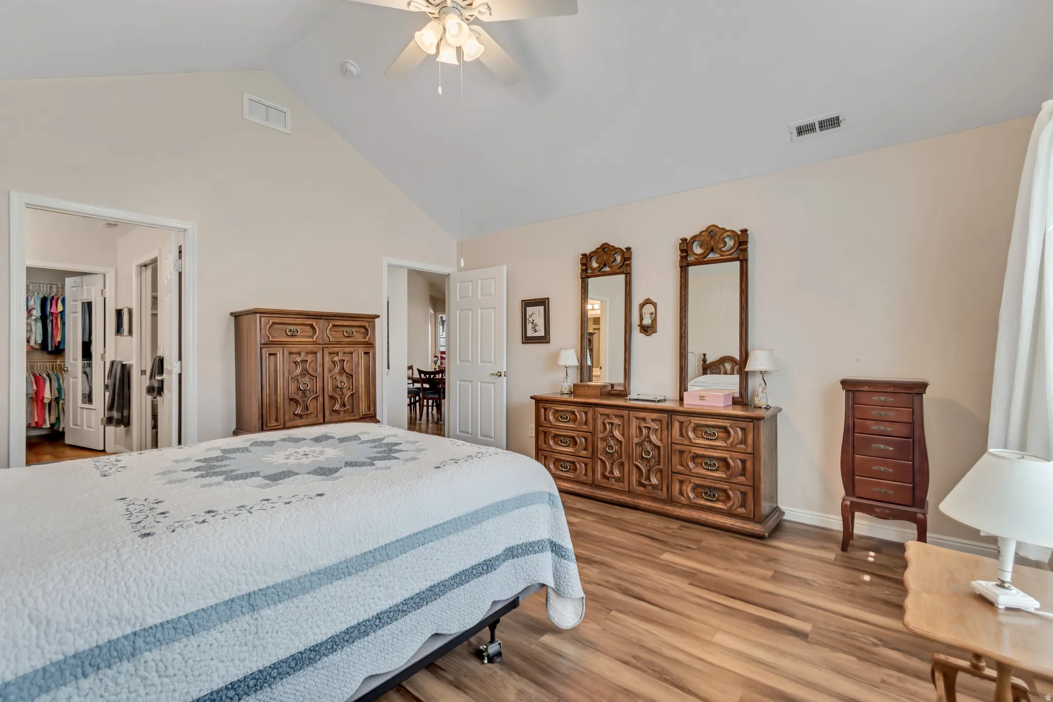 Spacious bedroom featuring vaulted ceilings, wood-finish flooring, a ceiling fan, and two doorways leading to other areas of the residence