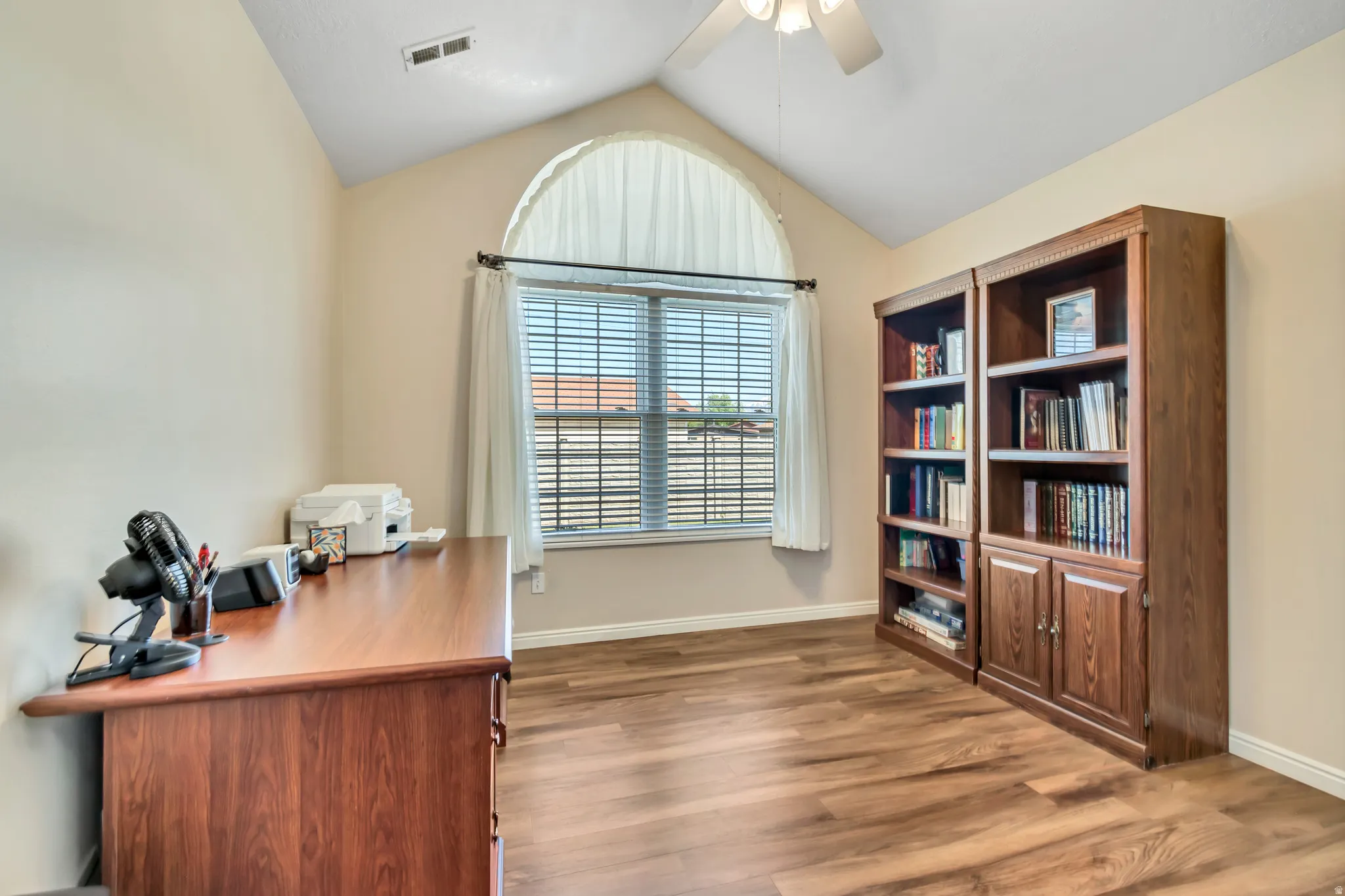 Bright home office featuring soaring vaulted ceilings with recessed lighting, arched transom window with plantation shutters, and rich wood-finish flooring